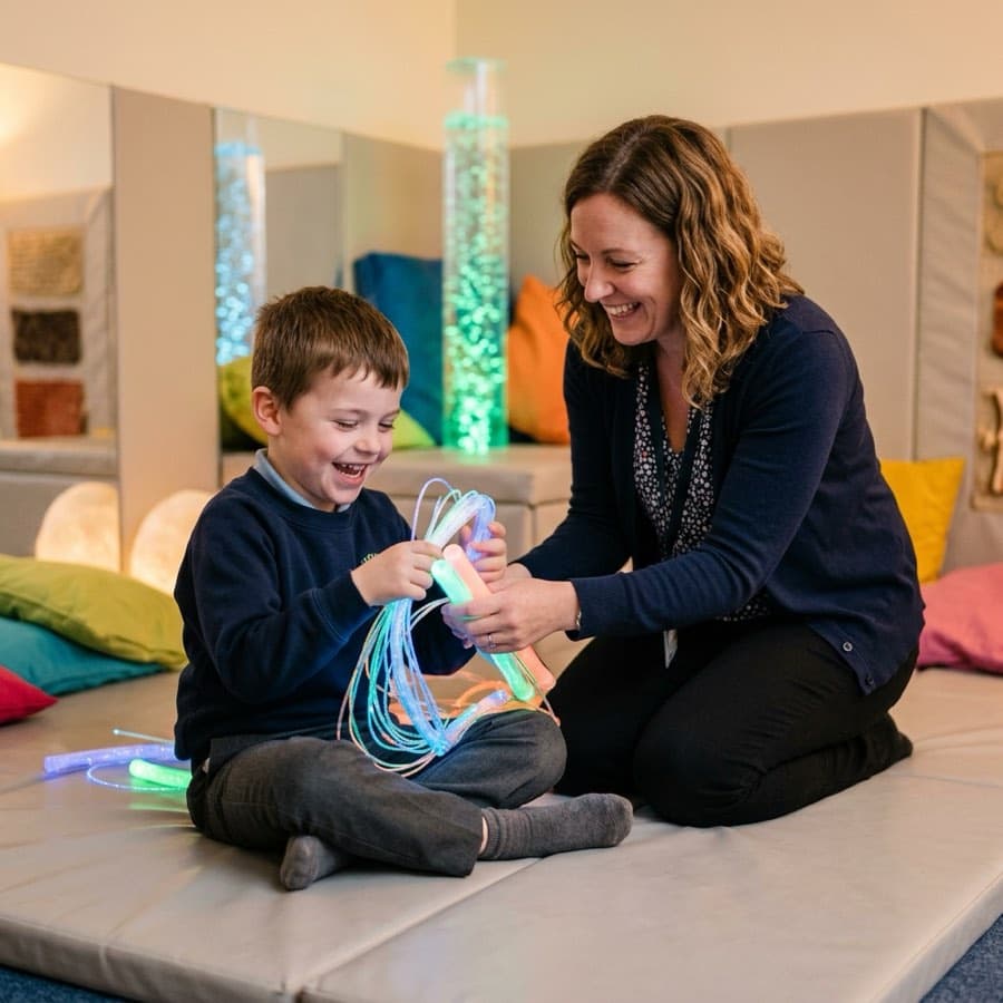 A child laughing with fibre-optic lights in a school sensory room